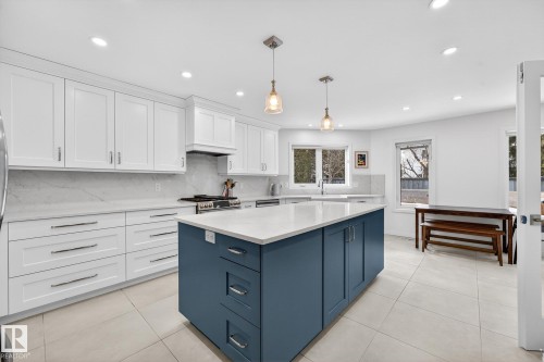 This kitchen features white cabinetry and a contrasting blue island with a white countertop - 1211 Hewgill Place, Edmonton, AB - Indoor Photo Showing Kitchen