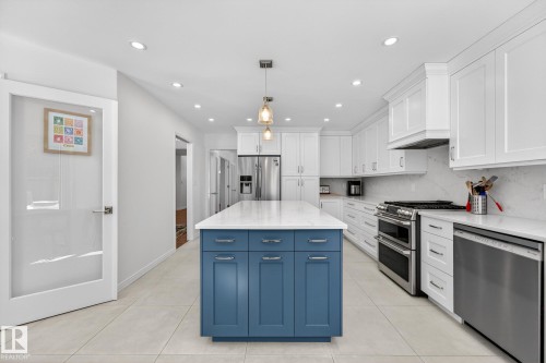 Spacious kitchen featuring white cabinetry, a blue central island with a light-colored countertop, and stainless steel appliances including a refrigerator, range, and dishwasher - 1211 Hewgill Place, Edmonton, AB - Indoor Photo Showing Kitchen With Upgraded Kitchen