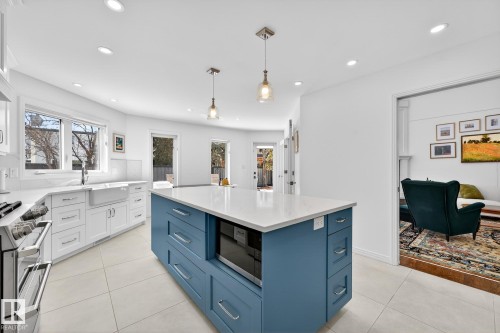 The kitchen features a blue island with a built-in microwave, white shaker-style cabinetry, and a farmhouse sink beneath a window - 1211 Hewgill Place, Edmonton, AB - Indoor Photo Showing Kitchen With Upgraded Kitchen