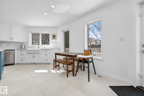 The kitchen features white cabinetry, stainless steel appliances, a farmhouse sink, and light-colored tile flooring - 1211 Hewgill Place, Edmonton, AB - Indoor