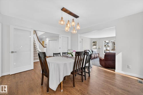 The property features hardwood floors, a contemporary light fixture, and a stairway with white risers and a wooden handrail - 1211 Hewgill Place, Edmonton, AB - Indoor Photo Showing Dining Room