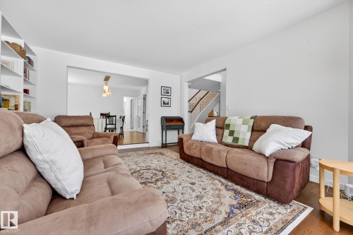 The living area features hardwood floors and a decorative area rug, with a built-in shelving unit providing storage and display space - 1211 Hewgill Place, Edmonton, AB - Indoor Photo Showing Living Room