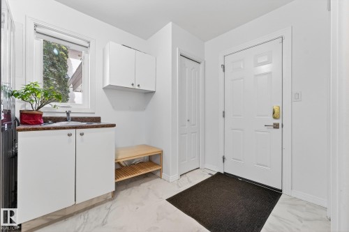 This mudroom features white cabinetry with a countertop and sink, a window, and a white door with a gold handle - 1211 Hewgill Place, Edmonton, AB - Indoor Photo Showing Other Room