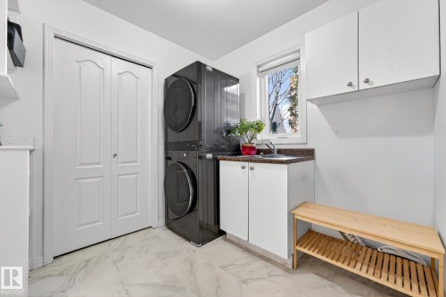 Laundry area featuring a stacked washer and dryer, white cabinetry, a sink with a dark countertop, and a window providing natural light - 1211 Hewgill Place, Edmonton, AB - Indoor Photo Showing Laundry Room