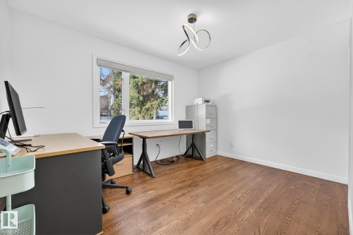 This room features rich hardwood flooring, a modern light fixture, and a large window providing views of exterior trees - 1211 Hewgill Place, Edmonton, AB - Indoor Photo Showing Office