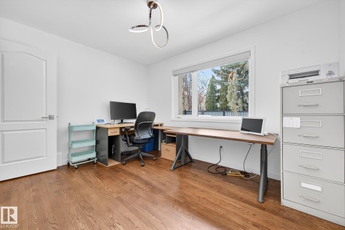 This room features hardwood floors, a large window providing natural light, a white paneled door, and a modern ceiling light fixture - 1211 Hewgill Place, Edmonton, AB - Indoor Photo Showing Office