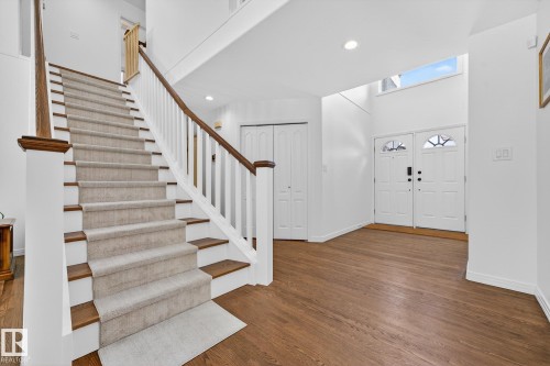 The property features an inviting entryway with rich hardwood flooring, a carpeted staircase with white risers and wood banisters, and a double entry door with decorative glass panels - 1211 Hewgill Place, Edmonton, AB - Indoor Photo Showing Other Room