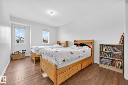 This room features two beds with natural wood frames, hardwood floors, and two windows providing natural light - 1211 Hewgill Place, Edmonton, AB - Indoor Photo Showing Bedroom