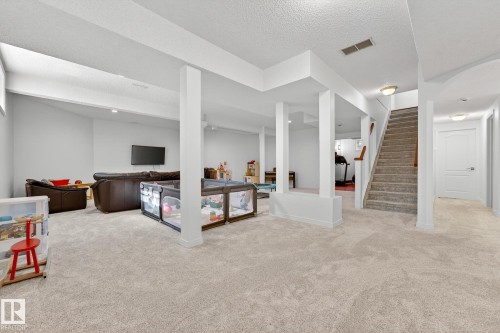 The property features a spacious room with light-colored carpeted floors, white walls, and a staircase with a wooden handrail - 1211 Hewgill Place, Edmonton, AB - Indoor