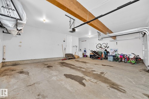 The property features a spacious garage with a concrete floor, exposed wooden beams, and a white overhead garage door - 1211 Hewgill Place, Edmonton, AB - Indoor Photo Showing Garage