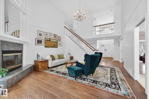 This spacious living area features hardwood floors, a fireplace with a stone surround, and a grand staircase with white balusters - 1211 Hewgill Place, Edmonton, AB - Indoor With Fireplace