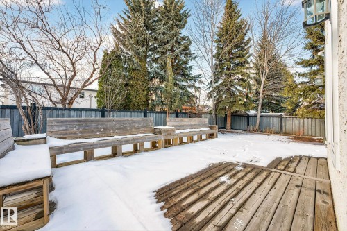 The property features a backyard with a wooden deck and built-in wooden benches, surrounded by a fence and mature trees - 1211 Hewgill Place, Edmonton, AB - Outdoor
