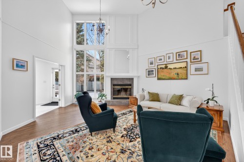 The living area features high ceilings, large windows providing natural light, and a fireplace with a mantel - 1211 Hewgill Place, Edmonton, AB - Indoor Photo Showing Living Room With Fireplace