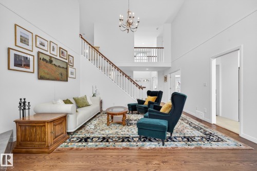 This living area features hardwood floors and a striking white staircase with a wooden handrail, leading to an upper landing - 1211 Hewgill Place, Edmonton, AB - Indoor Photo Showing Living Room