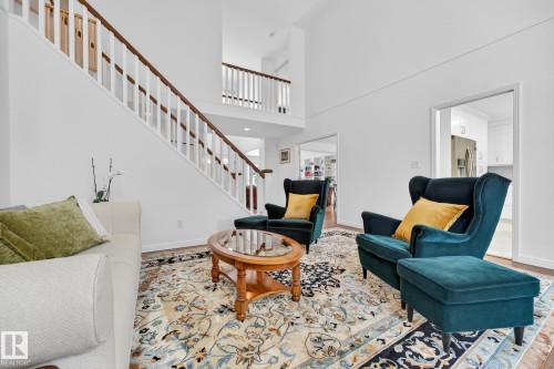 This living area features soaring ceilings and a staircase with white balusters and a dark wood handrail - 1211 Hewgill Place, Edmonton, AB - Indoor Photo Showing Living Room