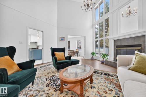 This expansive living area features towering ceilings, large windows that provide ample natural light, and a fireplace with a dark tile surround - 1211 Hewgill Place, Edmonton, AB - Indoor Photo Showing Living Room With Fireplace