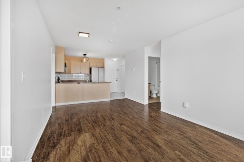 This bright living space features wood-style flooring, a kitchen with light wood cabinetry and stainless steel appliances, and a partial view of a bathroom - 105 4309 33 Street, Stony Plain, AB - Indoor