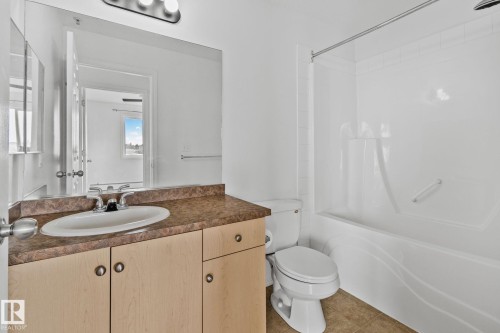 Bathroom with a vanity featuring a light brown countertop and an integrated sink, a toilet, and a bathtub with a showerhead - 105 4309 33 Street, Stony Plain, AB - Indoor Photo Showing Bathroom
