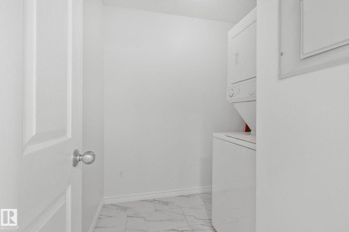 Dedicated laundry area featuring a stacked washer and dryer unit, white walls, and tiled flooring - 105 4309 33 Street, Stony Plain, AB - Indoor Photo Showing Laundry Room