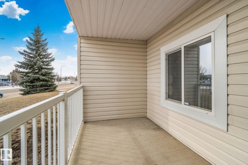 Outdoor balcony featuring light-colored siding, a white railing, and a window providing a view of the street and a large evergreen tree - 105 4309 33 Street, Stony Plain, AB - Outdoor With Exterior