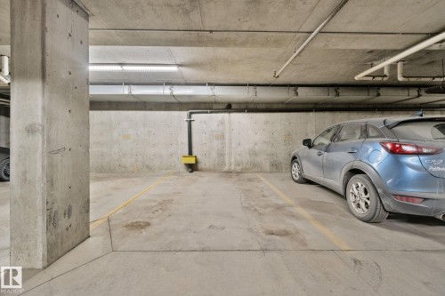 Dedicated parking space in a concrete parking garage, featuring overhead lighting and exposed utilities - 105 4309 33 Street, Stony Plain, AB - Indoor Photo Showing Garage