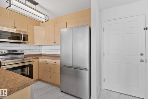 The kitchen features stainless steel appliances, light-toned cabinetry, and a white subway tile backsplash - 105 4309 33 Street, Stony Plain, AB - Indoor Photo Showing Kitchen
