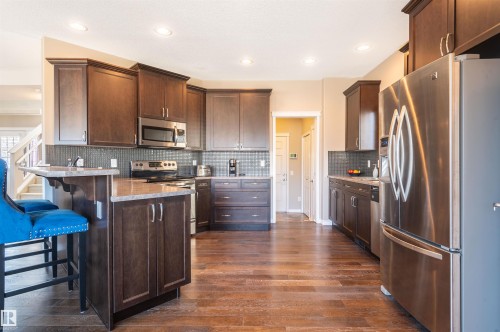 Kitchen featuring wood-finish flooring, dark wood cabinetry, a built-in microwave, stainless steel appliances, and recessed lighting - 121 Ellington Crescent, St. Albert, AB - Indoor Photo Showing Kitchen With Upgraded Kitchen