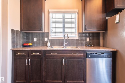 Kitchen featuring dark wood-finish cabinetry with silver hardware, speckled countertops, and a mosaic tile backsplash - 121 Ellington Crescent, St. Albert, AB - Indoor Photo Showing Kitchen With Double Sink