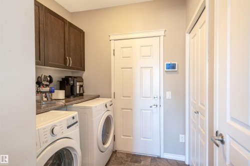 Dedicated laundry area featuring a white front-load washer and dryer set, dark wood-finish cabinetry, and a spacious countertop - 121 Ellington Crescent, St. Albert, AB - Indoor Photo Showing Laundry Room