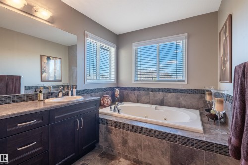 Spacious bathroom featuring a built-in jetted tub with tiled surround, a large vanity with an integrated sink, a wide mirror, and dual windows with blinds - 121 Ellington Crescent, St. Albert, AB - Indoor Photo Showing Bathroom