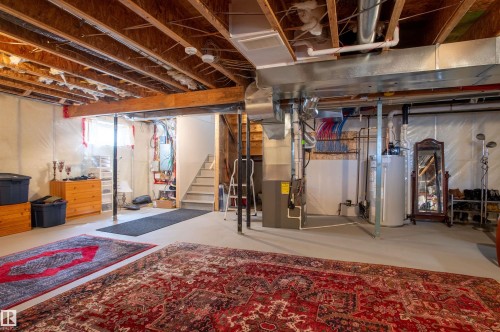 Unfinished basement featuring exposed wood joists and structural beams, a visible water heater, furnace, and utility piping, and a staircase providing access to an upper level - 121 Ellington Crescent, St. Albert, AB - Indoor Photo Showing Basement