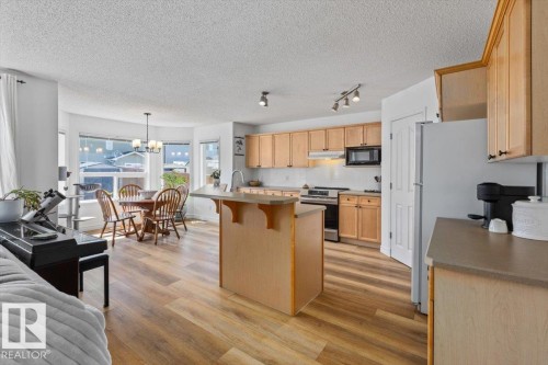 Spacious kitchen and dining area featuring wood-finish flooring, light wood cabinetry, stainless steel appliances, a kitchen island, and a dining area with a bay window - 1130 Westerra Way, Stony Plain, AB - Indoor Photo Showing Kitchen