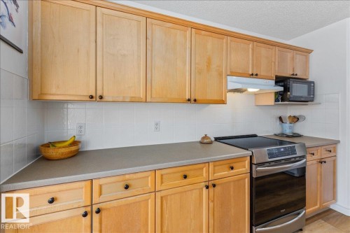 Kitchen featuring light wood cabinetry with dark hardware, solid surface countertops, white tile backsplash, and a stainless steel range - 1130 Westerra Way, Stony Plain, AB - Indoor Photo Showing Kitchen
