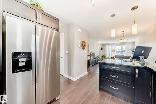 Kitchen featuring stainless steel side-by-side refrigerator, dark wood cabinetry, and wood-finish flooring - 115 401 Southfork Drive, Leduc, AB - Indoor Photo Showing Kitchen With Stainless Steel Kitchen