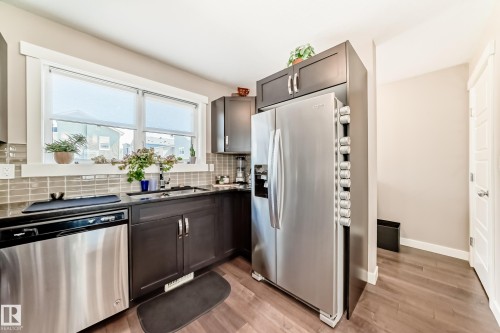 Kitchen featuring dark wood cabinetry, stainless steel appliances, a tile backsplash, and wood-finish flooring - 115 401 Southfork Drive, Leduc, AB - Indoor Photo Showing Kitchen With Stainless Steel Kitchen