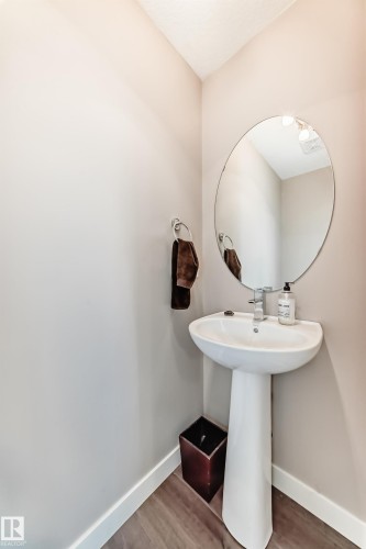 Compact powder room featuring a white pedestal sink, chrome faucet, and a round wall mirror - 115 401 Southfork Drive, Leduc, AB - Indoor Photo Showing Bathroom