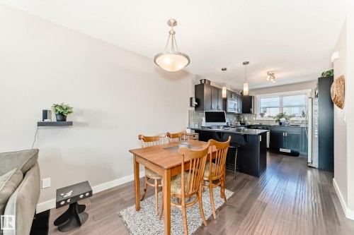 Open-concept kitchen and dining area featuring dark wood-finish flooring, a kitchen island with seating, dark cabinetry, and stainless steel appliances - 115 401 Southfork Drive, Leduc, AB - Indoor