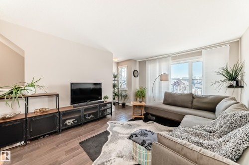 Living area featuring wood-finish flooring, a large window with vertical blinds, and neutral wall tones - 115 401 Southfork Drive, Leduc, AB - Indoor Photo Showing Living Room