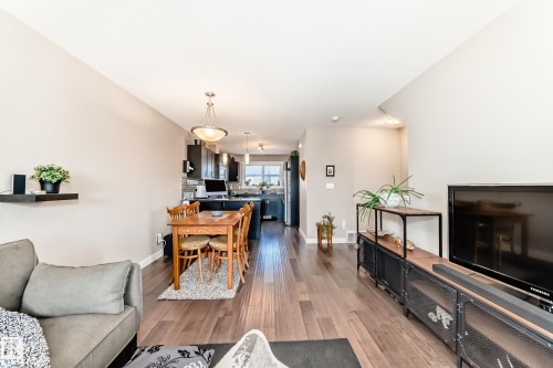 Open-concept living space featuring wood-finish flooring, a kitchen with dark cabinetry, and a dining area illuminated by a pendant light fixture - 115 401 Southfork Drive, Leduc, AB - Indoor Photo Showing Living Room