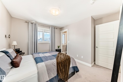 Bedroom featuring neutral tone walls, soft carpet flooring, and a large window with white trim - 115 401 Southfork Drive, Leduc, AB - Indoor Photo Showing Bedroom
