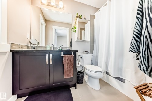 Bathroom featuring a dark wood-finish vanity with a black countertop, a rectangular mirror, and a three-bulb vanity light fixture - 115 401 Southfork Drive, Leduc, AB - Indoor Photo Showing Bathroom