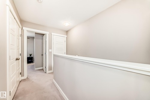 Carpeted hallway featuring multiple paneled doors with white trim, a half-wall partition, and ceiling-mounted lighting - 115 401 Southfork Drive, Leduc, AB - Indoor Photo Showing Other Room