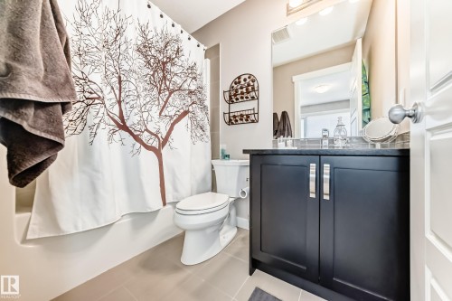 Bathroom featuring a dark wood vanity with brushed nickel hardware, a rectangular vanity mirror, and a sleek white toilet - 115 401 Southfork Drive, Leduc, AB - Indoor Photo Showing Bathroom