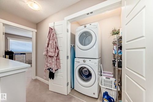 Dedicated laundry area with stacked washer and dryer appliances, neutral wall paint, and overhead lighting - 115 401 Southfork Drive, Leduc, AB - Indoor Photo Showing Laundry Room