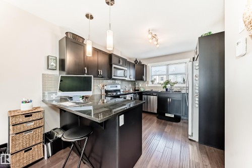 Kitchen featuring dark wood-finish cabinetry, stainless steel appliances, a grey tile backsplash, and wood-finish flooring - 115 401 Southfork Drive, Leduc, AB - Indoor Photo Showing Kitchen