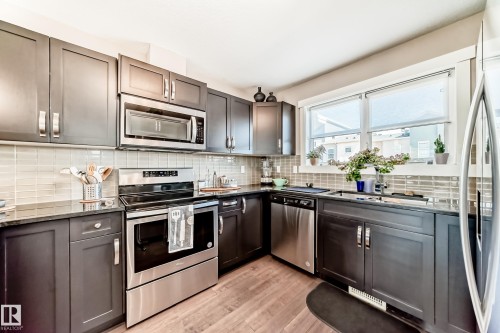 Kitchen featuring dark cabinetry, stainless steel appliances, granite countertops, a tiled backsplash, and wood-finish flooring - 115 401 Southfork Drive, Leduc, AB - Indoor Photo Showing Kitchen With Stainless Steel Kitchen With Upgraded Kitchen