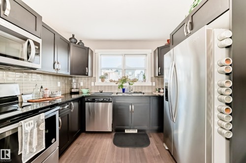 Modern kitchen featuring dark wood-finish cabinetry, stainless steel appliances, dark countertops, and a subway tile backsplash - 115 401 Southfork Drive, Leduc, AB - Indoor Photo Showing Kitchen With Stainless Steel Kitchen With Upgraded Kitchen