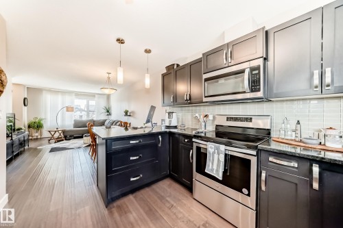 Modern kitchen featuring dark cabinetry, stainless steel appliances, a tile backsplash, and an island with pendant lighting - 115 401 Southfork Drive, Leduc, AB - Indoor Photo Showing Kitchen With Stainless Steel Kitchen With Upgraded Kitchen