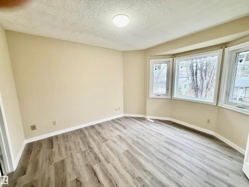 Room featuring a multi-pane bay window, wood-finish flooring, light-toned wall paint, and a ceiling-mounted light fixture - 10905 74 Avenue, Edmonton, AB - Indoor Photo Showing Other Room
