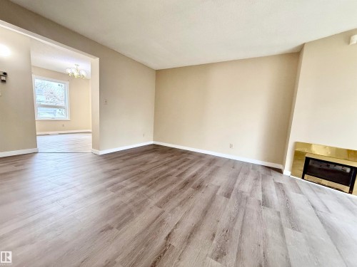 Living area featuring wood-finish flooring and a fireplace with a brass-toned surround - 10905 74 Avenue, Edmonton, AB - Indoor With Fireplace